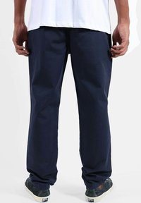 Pantalon bleu marine en coton, doté d'une coupe droite et d'une texture lisse, associé à une chemise blanche et des chaussures décontractées.