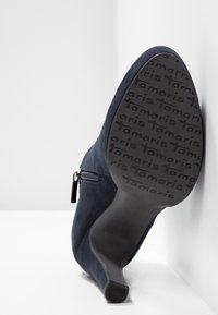 Bottine à talon en suédine marine à bout pointu avec fermeture éclair latérale, semelle marquée "Tamaris," taille 37, photographiée par le dessous sur fond blanc.