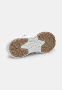 Suola di sneaker bianca con battistrada in gomma marrone, caratterizzata da profondi motivi a zigzag e aree di presa texture su uno sfondo bianco.
