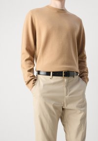 Maglione di lana beige con scollatura a girocollo, abbinato a pantaloni beige chiaro. Cintura in pelle nera con dettaglio della fibbia dorata inclusa.