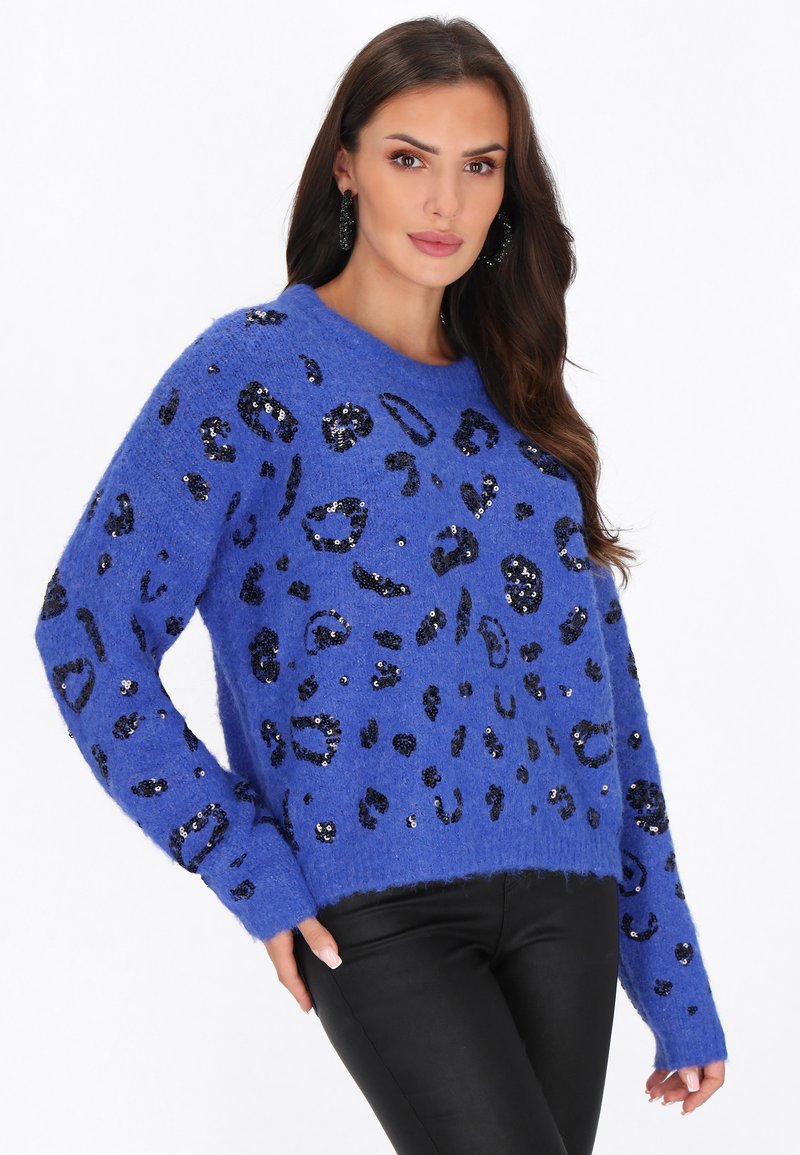 Zils pūkains džemperis ar melnu secinātu leopardu rakstu, ribotām aprocēm un noapaļotu kaklu, saderībā ar pieguļošām melnām biksēm.