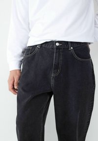 Czarne dżinsy o prostym kroju nogawki, z widocznymi detalami szwów, kieszeniami z przodu oraz zapięciem na guzik w pasie.