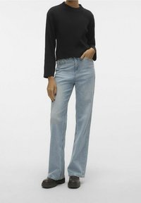 Maglione nero a coste con maniche lunghe abbinato a jeans a vita alta di colore blu chiaro. Il modello indossa stivali scuri con suola spessa. Design semplice e pulito.