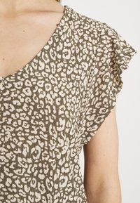 Top de manga corta en verde olivo con un estampado de animales en blanco. Presenta un escote en V y bordes de mangas con volantes para mayor textura.