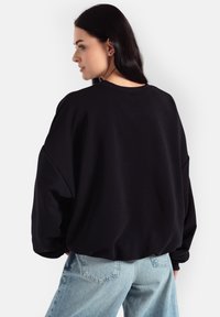 Czarny oversize bluza z dzianiny o prążkowanej fakturze, okrągłym dekoltem i opuszczonymi ramionami, w połączeniu z jasnoniebieskimi jeansami z wysokim stanem.