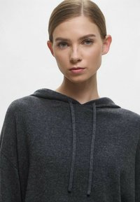 Felpa con cappuccio in morbido tessuto grigio scuro, con scollatura leggermente arrotondata, cordini frontali e una vestibilità ampia, progettata per il comfort e il relax quotidiano.