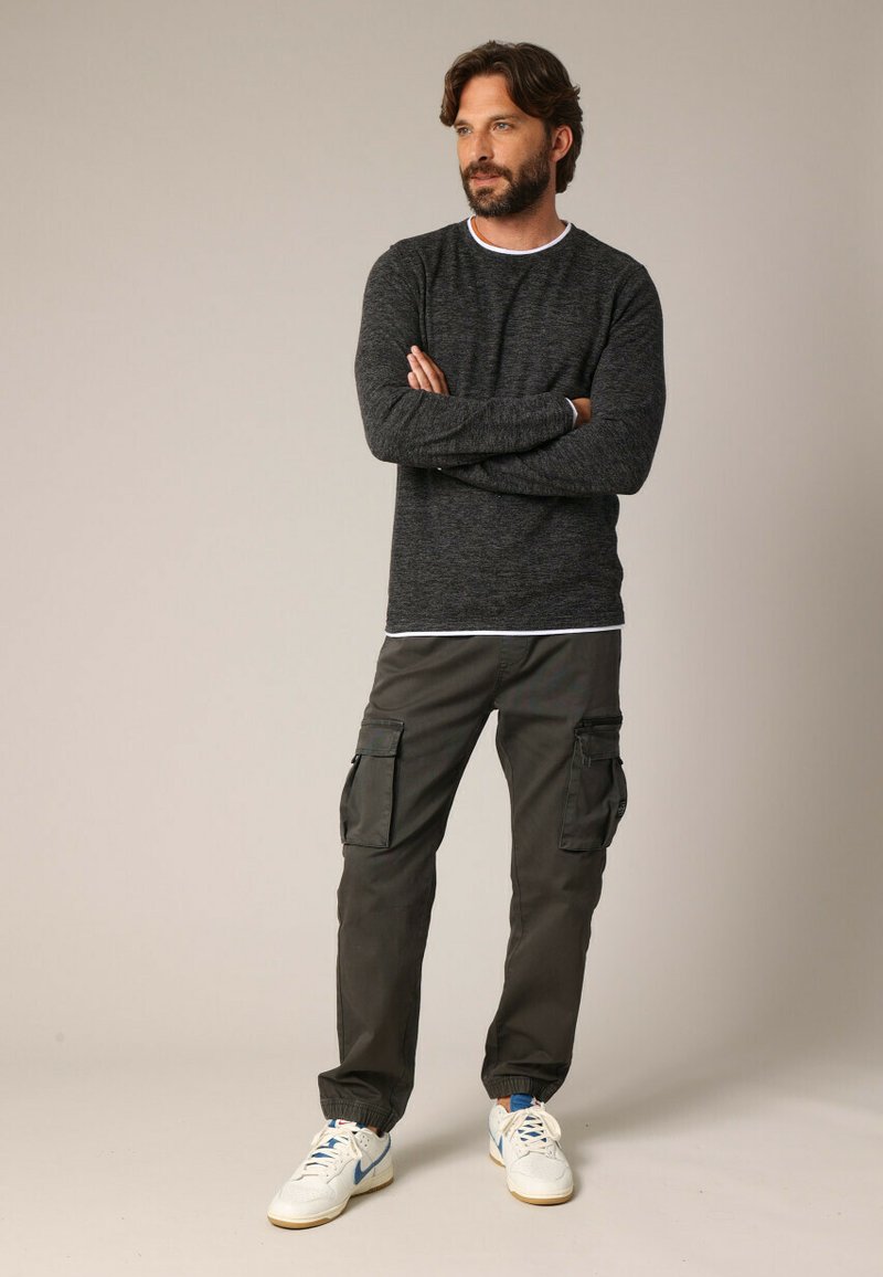 Donkergrijze sweater met lange mouwen en een witte binnenkraag, gecombineerd met cargobroeken met zakken en witte sneakers met blauwe accenten.