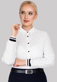 White long-sleeve shirt with black buttons and striped black and white cuffs, paired with a black belt, featuring a smooth fabric texture.