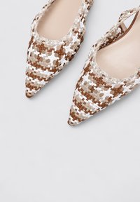 Zapatos de punta afilada tejidos, hechos de materiales en tonos marrón, beige y blanco, con un diseño de tobillo y una superficie texturizada.