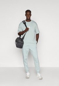 Gaiši zils kokvilnas T-krekls ar vaļēju fitu, kopā ar saskaņotām sporta biksēm. Melna soma ar logotipu, baltas sporta kurpes ar pelēkiem akcentiem.