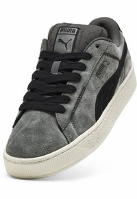 Sneaker in suede grigio con accenti neri, dotate di lacci rotondi, una suola in gomma testurizzata e un logo PUMA sulla linguetta e sul lato.