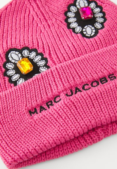 Klart rosa stickad mössa med svarta och vita blommotippar som har gula och rosa stenar, samt svart broderad text "MARC JACOBS".