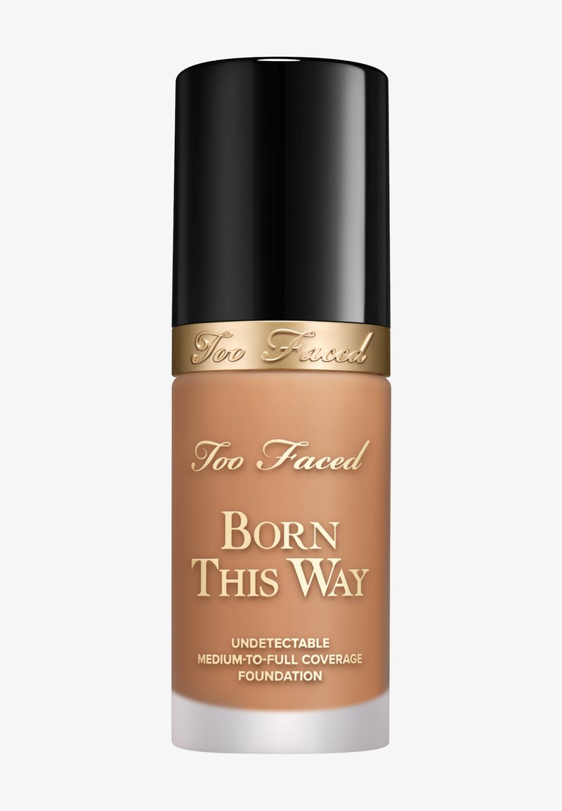 Too Faced Born This Way Foundation in einer Glasflasche mit schwarzem Deckel. Hellbraune Farbe; goldene Schrift auf dem Etikett. Glatte Textur.