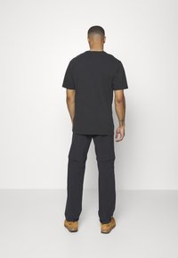 Zwarte korte mouwen T-shirt en donkere cargobroek, gezien van achteren. De broek heeft meerdere zakken en wordt gedragen met lichtbruine laarzen.
