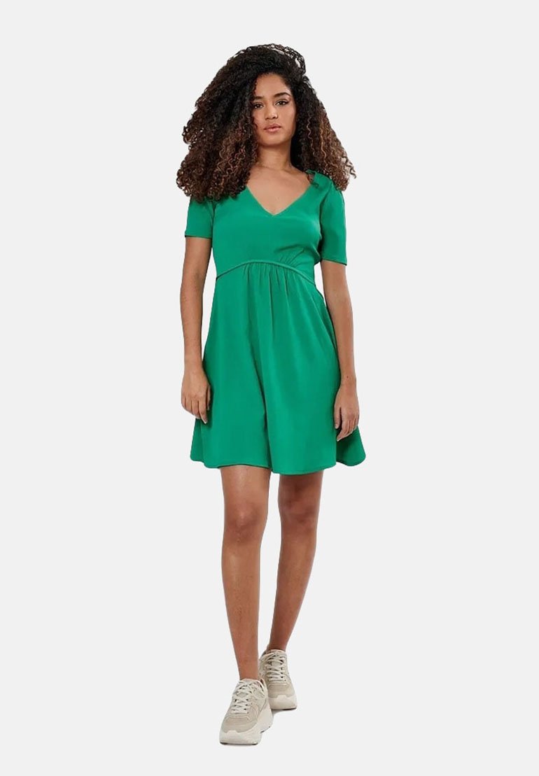 Groene jurk met korte mouwen en V-halslijn, gathered taille, vloeiende rok en een gestructureerde stof; gecombineerd met beige sneakers.