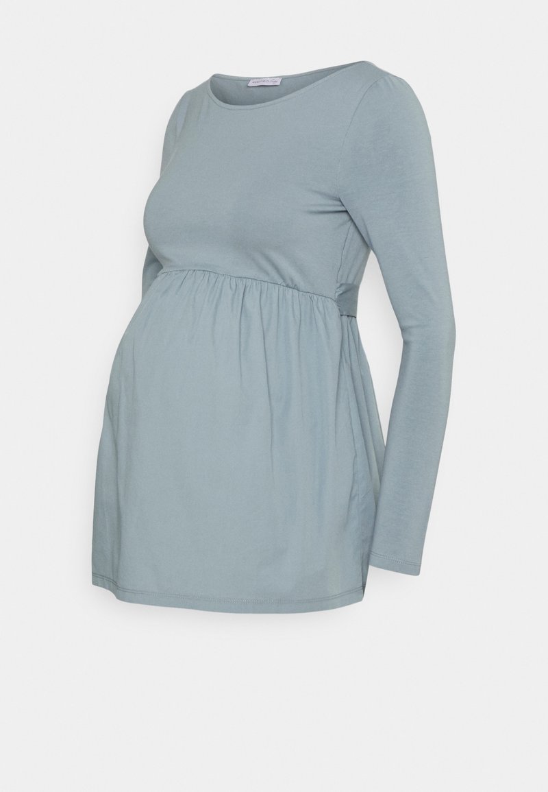 Těhotenský top z měkké, světle modré látky. Má dlouhé rukávy a nařasený pas pro větší volnost a pohodlí. Jednoduchý a prodyšný design.