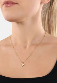 Collana d'oro con una catena sottile e un piccolo pendente angolare a forma di lettera "V". Design minimalista su una maglietta nera.