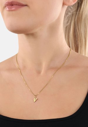 Collana d'oro con una catena sottile e un piccolo pendente angolare a forma di lettera "V". Design minimalista su una maglietta nera.