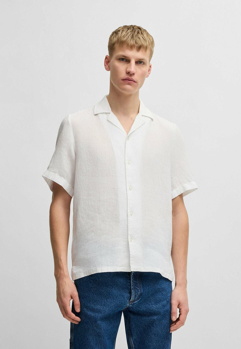 Witte linnen shirt met korte mouwen, een klassieke kraag, knoopsluiting aan de voorkant en een ontspannen pasvorm. Gecombineerd met blauwe denimjeans.