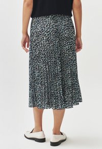 Jupe plissée en tissu sombre avec un motif de pois multicolores, dotée d'une taille élastique et d'une coupe longueur cheville. Chaussures blanches visibles.
