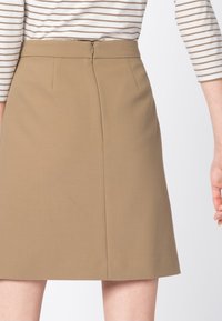 Gonna A-line beige con una superficie liscia, dotata di una cerniera sul retro e due pence frontali per una forma e un dettaglio aggiuntivi.