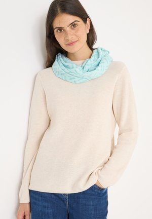 Lichtblauwe, gemusterde infinitiesjaal van zachte stof, gedragen over een beige geribde trui, gecombineerd met blauwe jeans.