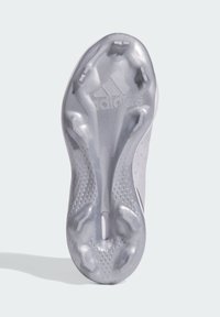 Suela de botín de fútbol metálica plateada con un agarre texturizado, que presenta múltiples clavos salientes y un logotipo grabado en la superficie.