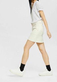 Blusa blanca de manga corta con lunares, combinada con una falda de mezclilla beige clara y zapatillas blancas, mostrando un atuendo casual y moderno.