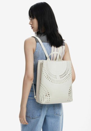 Zaino in pelle bianca perforata con design a intaglio, forma rettangolare, manico superiore e spallacci regolabili.