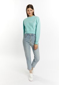 Licht turquoise cropped sweatshirt met een ronde hals en lange mouwen, gecombineerd met hoge lichtblauwe jeans en witte sneakers.