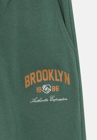 Grüner Sweatshirt mit braunem, gedrucktem "BROOKLYN 1986" -Text und weißer Stickerei "Authentis Expresium". Hergestellt aus weichem Baumwollmaterial.
