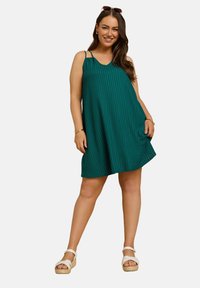 Tealrandig sommarklänning med tunna remmar, avslappnad form och knä-lång fåll. Bärs med vita kilklacksandaler för en avslappnad look.