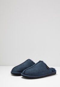Marineblå tøffel lavet af blødt ruskind med en fuzzy foring, åben hældesign og en tekstureret sål for bedre greb.