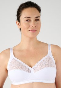 Sujetador blanco con paneles de encaje, material suave, bordes festoneados y tirantes ajustables, diseñado para comodidad y soporte.