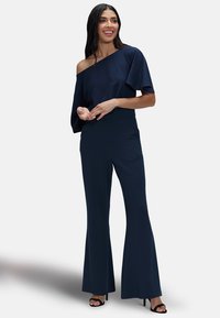 Een marineblauwe off-shoulder top met fladdermouwen, gecombineerd met hoge taille flare broeken, beide in een soepele, lichte stof.