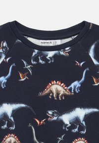 Φούτερ με μακριά μανίκια σε σκούρο μπλε ύφασμα με πολύχρωμα σχέδια δεινοσαύρων, συμπεριλαμβανομένων T-rex, στεγόσαυρου και πτεροσαύρων.