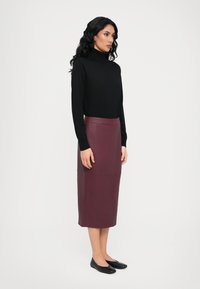 Haut noir à manches longues avec col roulé associé à une jupe midi en simili cuir bordeaux. Coupe ajustée ; texture lisse ; ballerines noires plates.