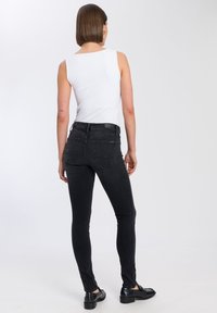 Czarne spodnie dżinsowe z wysokim stanem i dopasowanym krojem, z tylnymi kieszeniami i gładką powierzchnią, w zestawieniu z dopasowanym białym topem na ramiączkach.