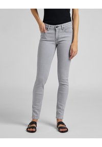 Jeans ajustados grises con cierre de botón, bolsillos frontales y una textura suave. Estilizados con sandalias negras de slides.