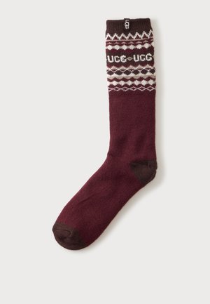 Jedna bordowa skarpetka z ciemnobrązowym palcem i piętą, z białymi i ciemnobrązowymi geometrycznymi wzorami oraz logo "UGG" blisko ściągacza.