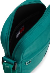 Τσάντα χιαστί σε τιρκουάζ χρώμα με υφή που μοιάζει με πλέγμα· κλείσιμο με φερμουάρ· εσωτερικά διαθέτει μαύρη επένδυση και ετικέτα με το εμπορικό σήμα. Ρυθμιζόμενο λουράκι.