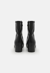 Bottines en cuir noir avec un talon épais, dotées d'une fermeture éclair et de coutures en relief le long des seams. Fini de surface lisse.