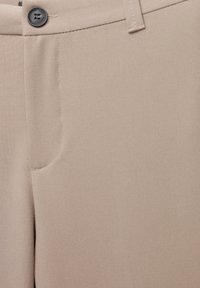Pantalon beige en tissu lisse, avec une fermeture à bouton unique, poche avant et design à jambe droite avec de subtils détails de couture.