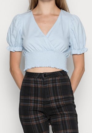 Top corto azul claro con escote en V y mangas abullonadas, que presenta una cinturilla fruncida. Combinado con pantalones de cuadros negros de cintura alta.