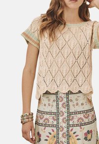 Jersey de color beige claro con patrones de diamante y dobladillo en forma de concha. Mangas cortas a rayas multicolores. Combinado con una falda de estampado floral.