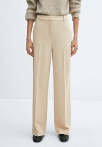 Lange beige broek gemaakt van lichtgewicht stof, met voorplooien en een op maat gemaakte tailleband voor een gestructureerde pasvorm.