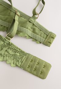 Rohelise pitsi ja kangaga rinnahoidja, millel on reguleeritavad sangad, sakilised servad ja konksudega kinnis. Omaduseks on tekstureeritud disain ja metallikaktsendid.