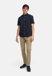 Marineblå kortermet skjorte med knapper, khaki chinos og mørke joggesko. Skjorten har krage og frontknapper. Enkel design uten mønstre.