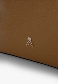 Lædertaske i tan med et forhøjet sølv skull og tværben logo. Teksturfinish med sort kant, der understreger håndværk og design.