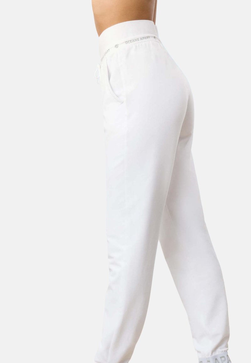 Białe dresy z elastycznym paskiem na sznurku, bocznymi kieszeniami i ściągaczami przy nogawkach. W pasie znajduje się tłoczone hasło "OCEANS APART".